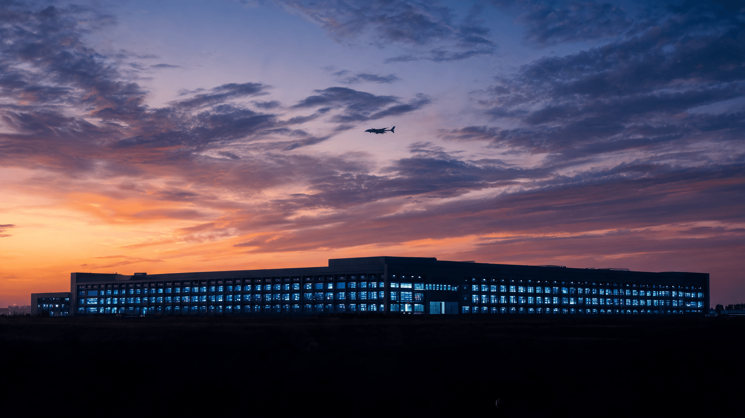A modern, sleek data center building silhouette under a dramatic sky with a subtle military-drone-th